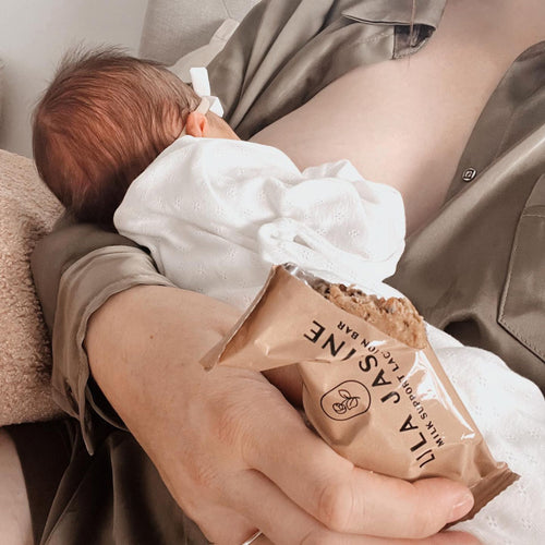 Mum breastfeeding newborn with one of Lila Jasmine's breastmilk support lactation bars in hand. Individually wrapped so you can eat on-the-go.