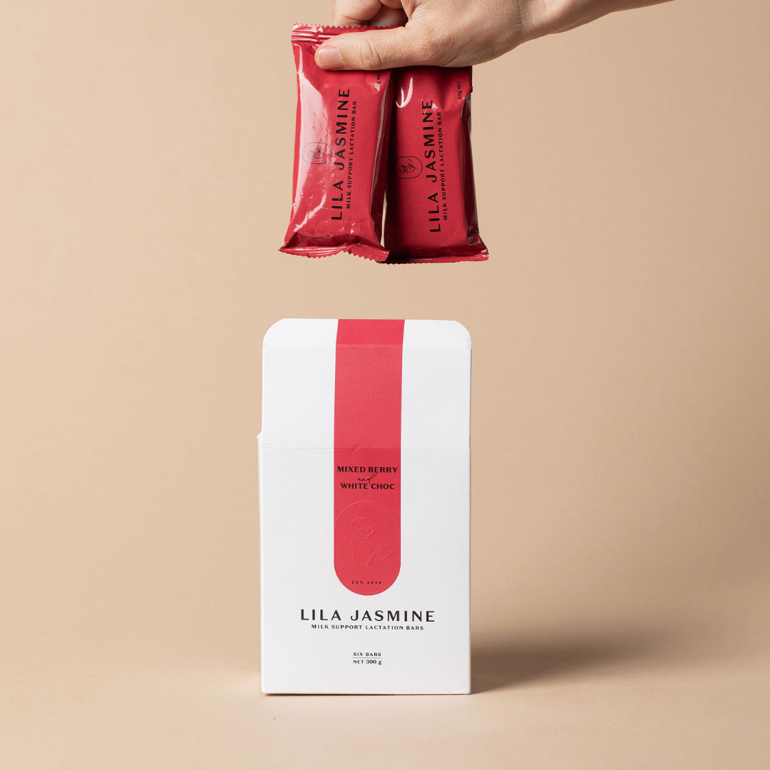 Hand holding Mixed Berry & White Chocolate Lila Jasmine lactation bars out of a outer white packaging box on a beige background