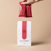 Hand holding Mixed Berry & White Chocolate Lila Jasmine lactation bars out of a outer white packaging box on a beige background