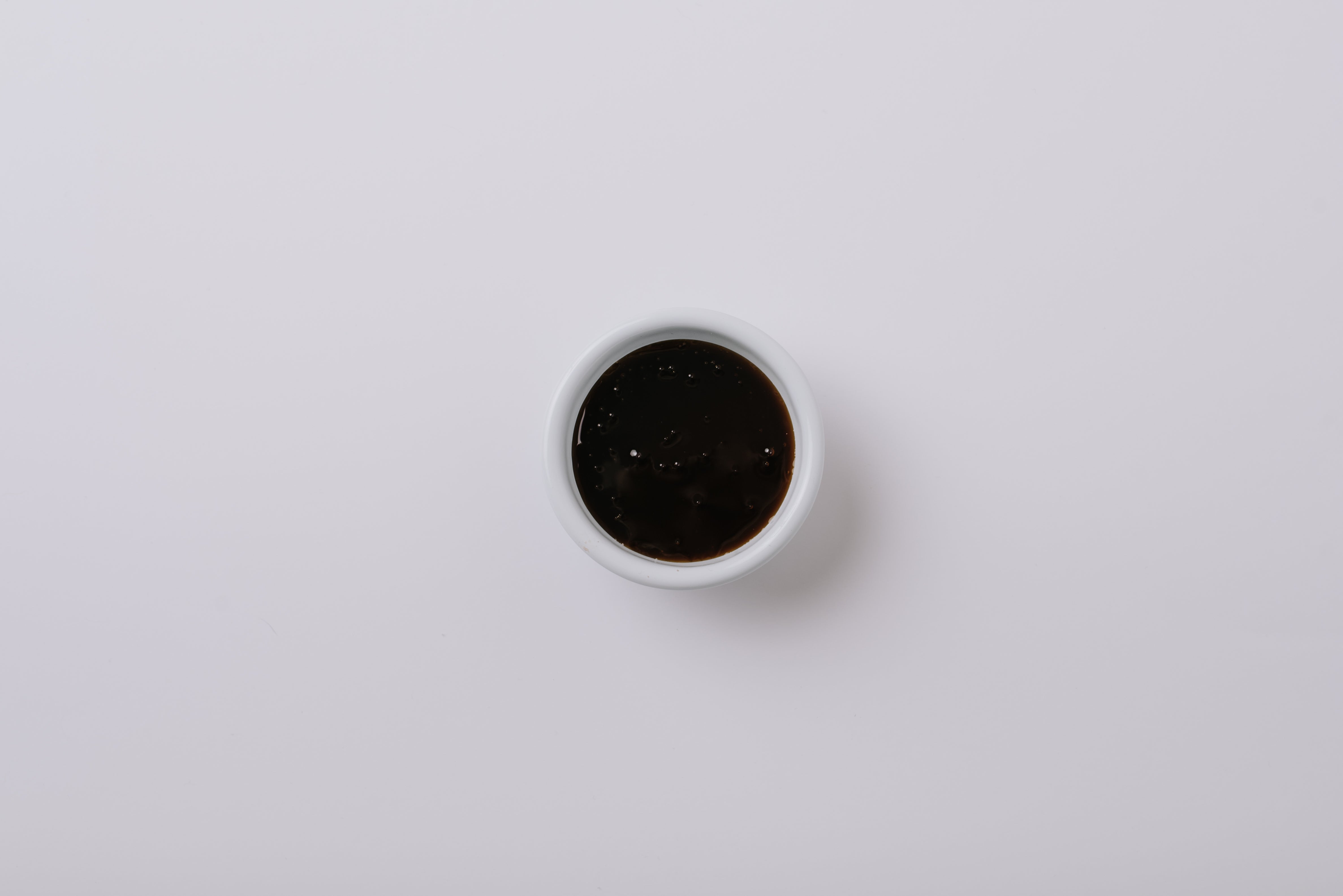 Small white bowl filled with golden syrup a light grey background