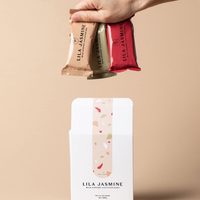 Hand holding Lila Jasmine milk support lactation bars against a beige background