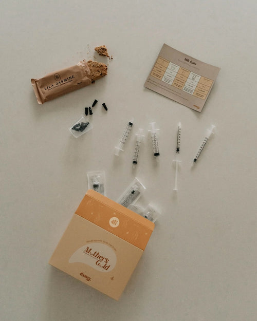 Collection of colostrum collection supplies including syringes and a box labeled 'Mother's Gold' on a light surface.