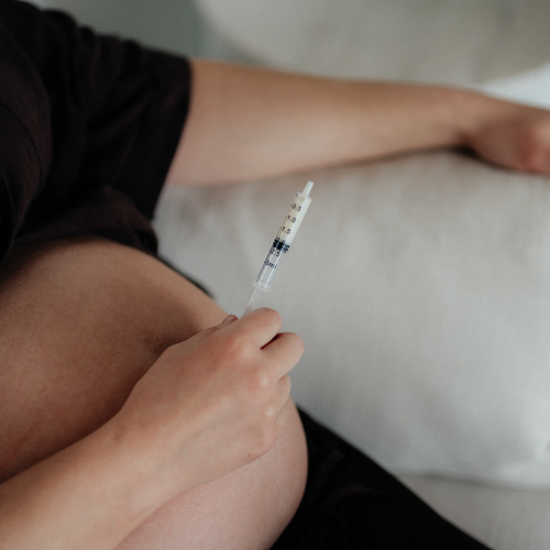Pregnant person holding a syringe with expressed antenatal colostrum with a blurred background