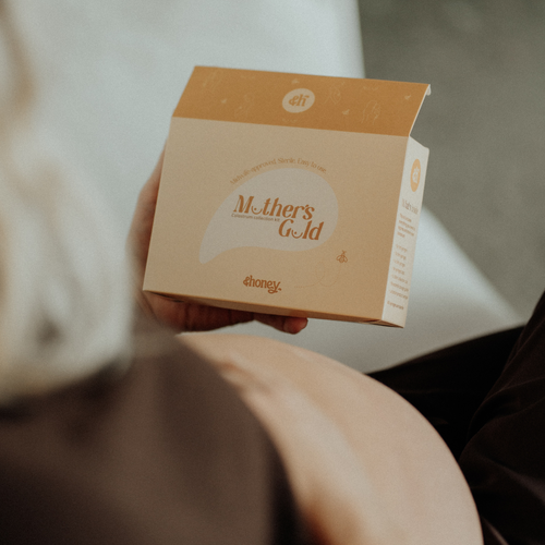 Pregnant person holding a box labeled 'Mother's Gold Colostrum Collection Kit' with a blurred background