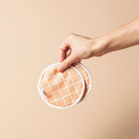 Hand holding a reusable Bear & Moo breast pad on a beige background